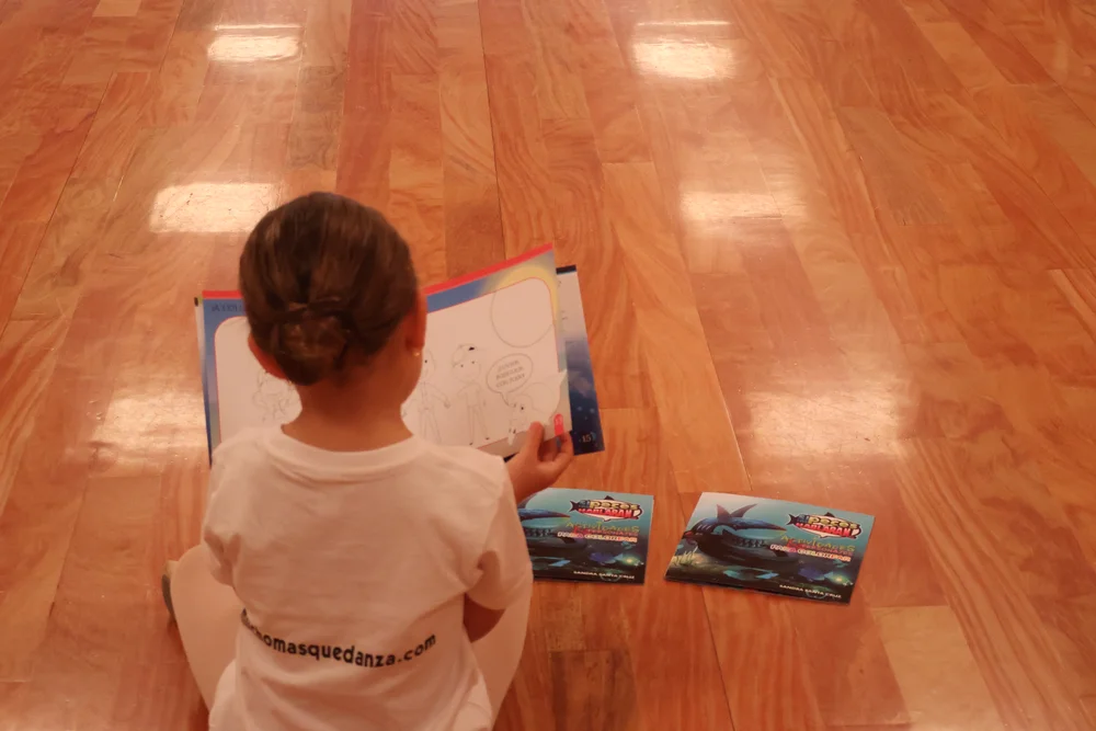Niña sentada en el suelo con el cuadernillo de actividades abierto