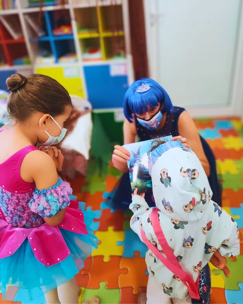 Niñas de la compañía leyendo el cuento con una pequeña paciente en la sala de juegos del hospital