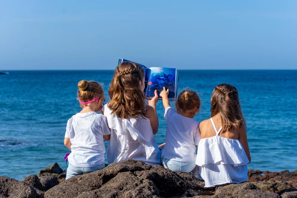 Cuatro niñas leyendo juntas el cuento sentadas en las rocas frente al mar